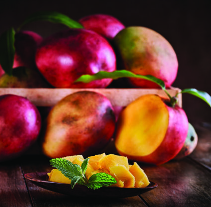 Tropical fruits. Group of ripe mangos on a crate in rustic table with mango slice.